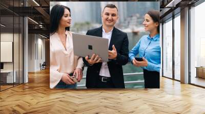 Focused business people reading news on laptop outdoors. Business people wearing formal clothes with buildings in background. Business work concept. Wall mural